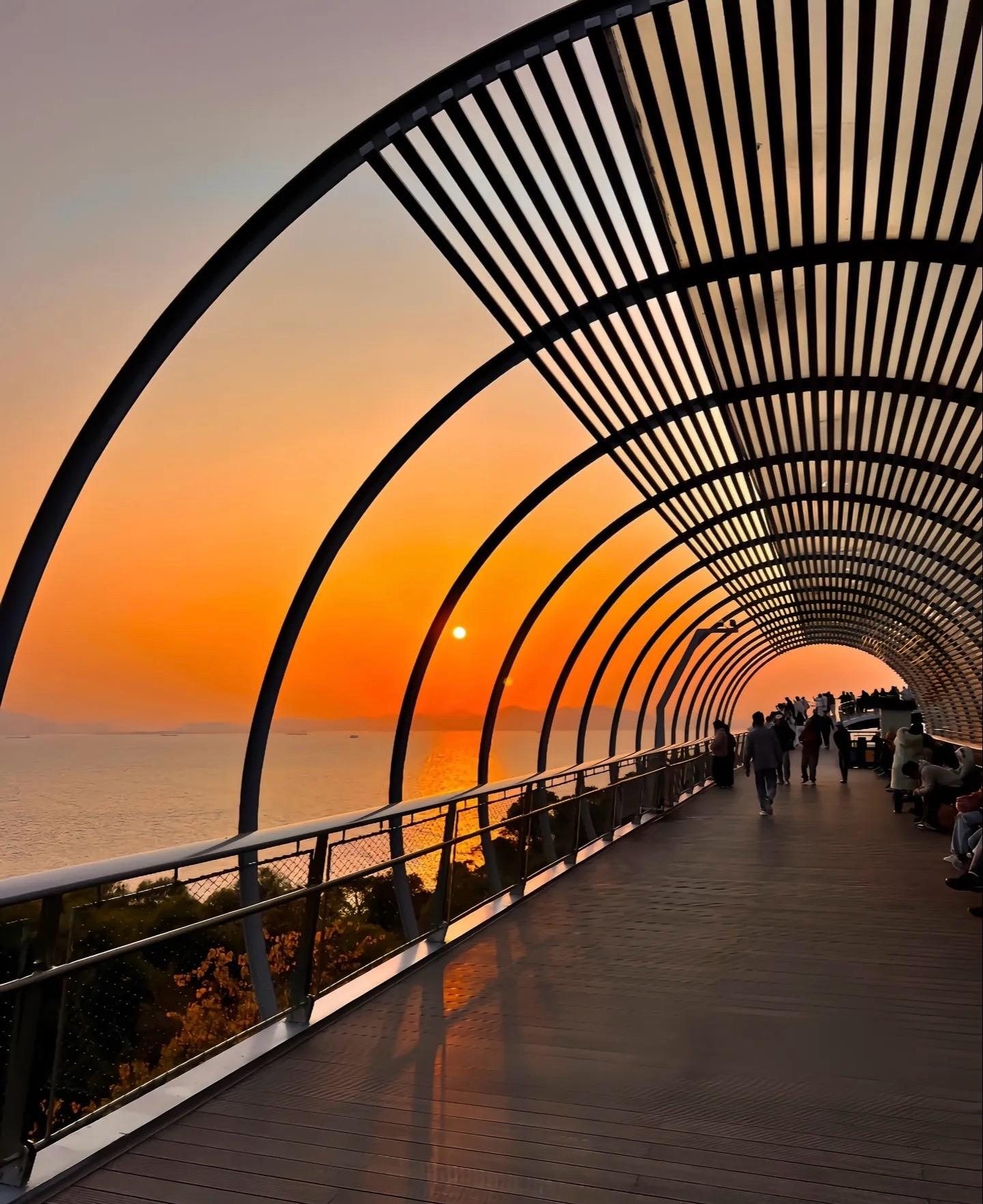Covered seaside walkway in Xiamen at sunset, with people strolling along the coast
