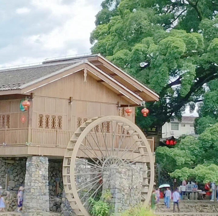 A wooden water wheel beside an old timber house under banyan trees at Yunshuiyao